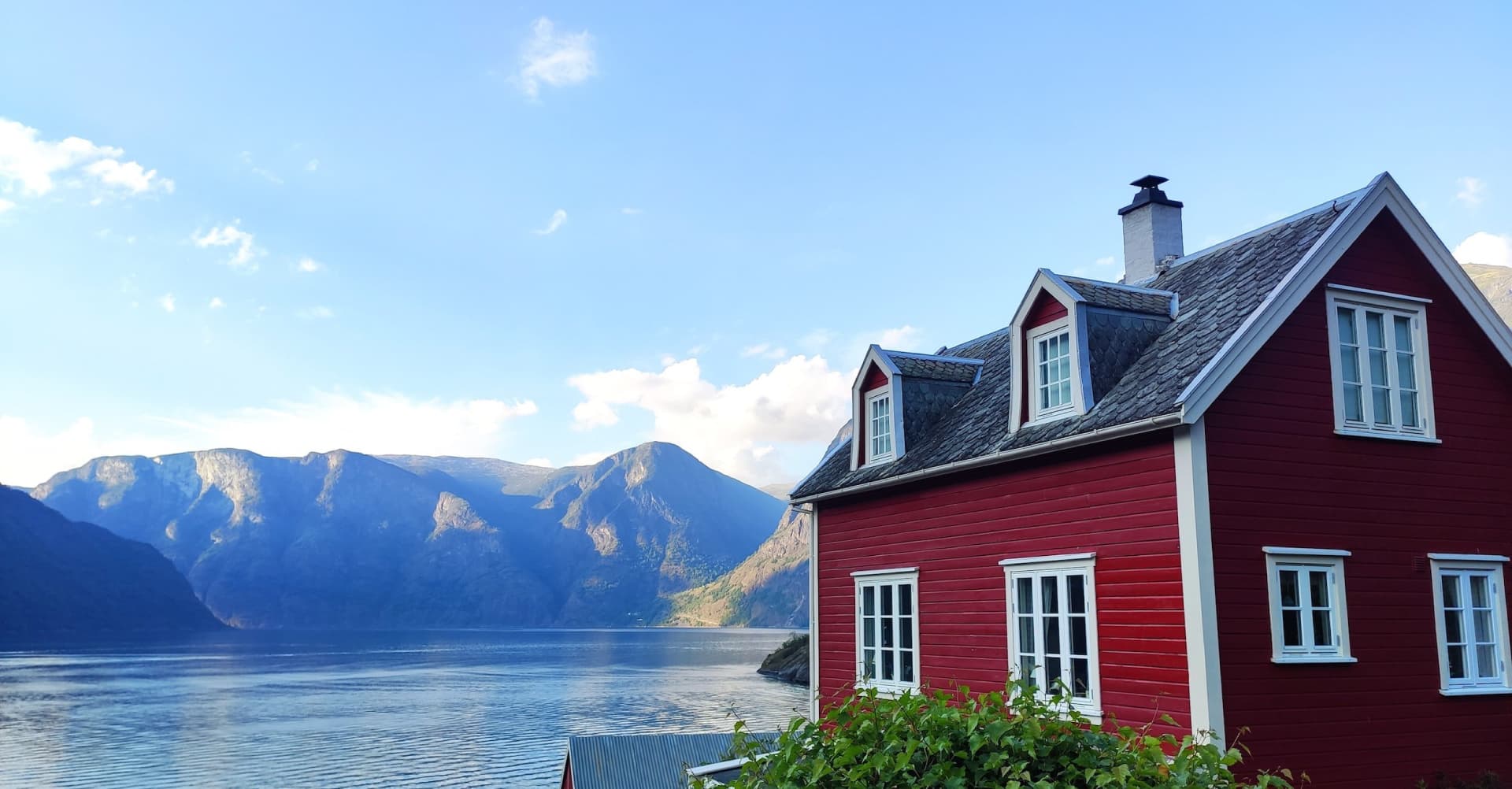 Maison en bord de fjord avec bardage bois avec une lasure rouge.